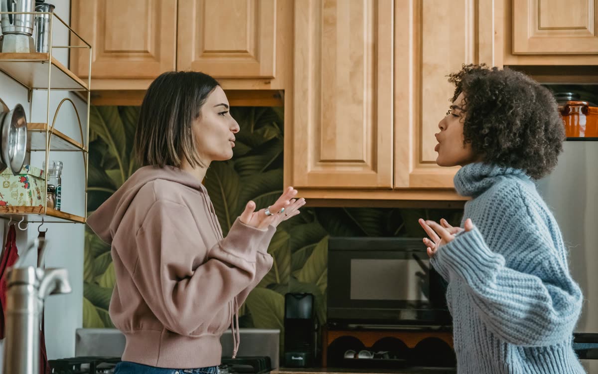 Two people in a kitchen mid-conversation, both gesturing 'I don't know'